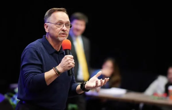 Dennis Buttimer holding a microphone speaks at an event, with another person in the background.