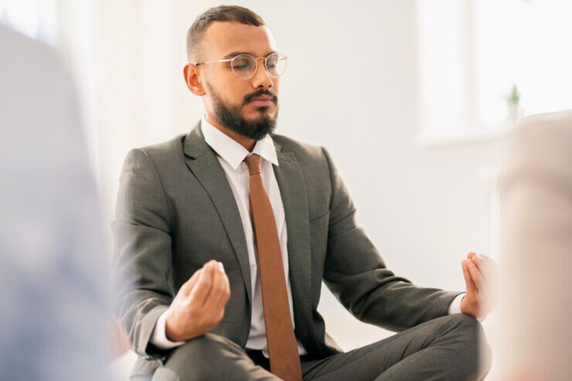 A man in monk mode, meditating with closed eyes and hands in a mudra position, seated indoors.