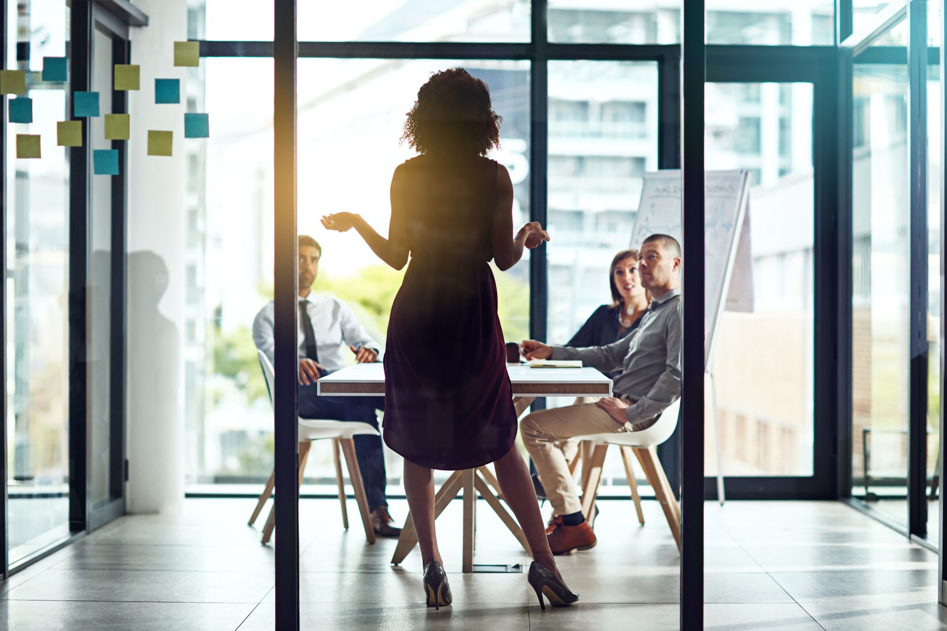 A woman demonstrates leadership as she presents to a group of colleagues in a modern office setting.