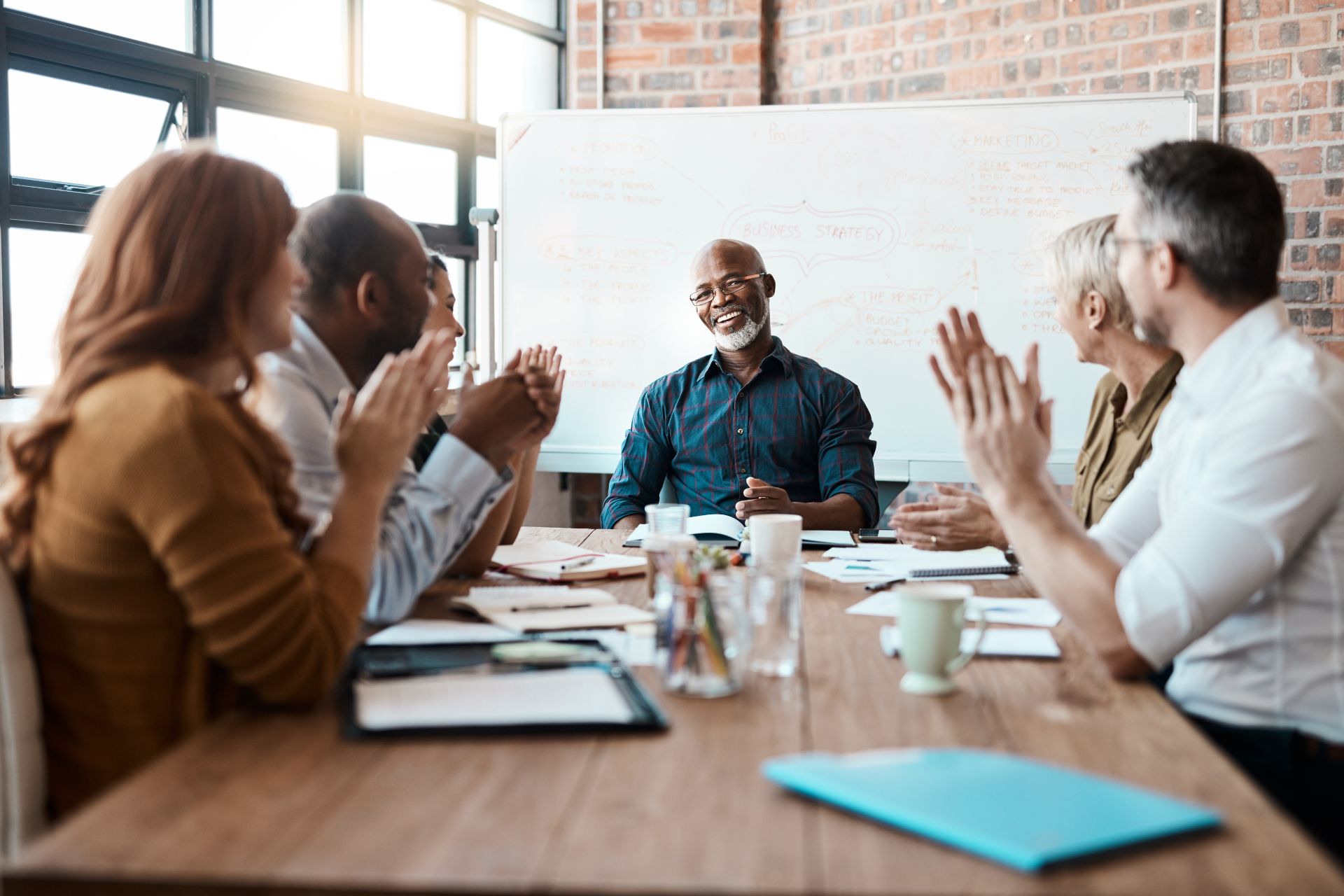 A group of professionals engaged in a discussion on effective leadership and applauding at a conference table.