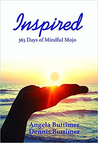 Book cover of "Inspired: 365 Days of Mindful Mojo" available in store, featuring a silhouetted hand against a sunset over the ocean with authors' names, Angela and Dennis