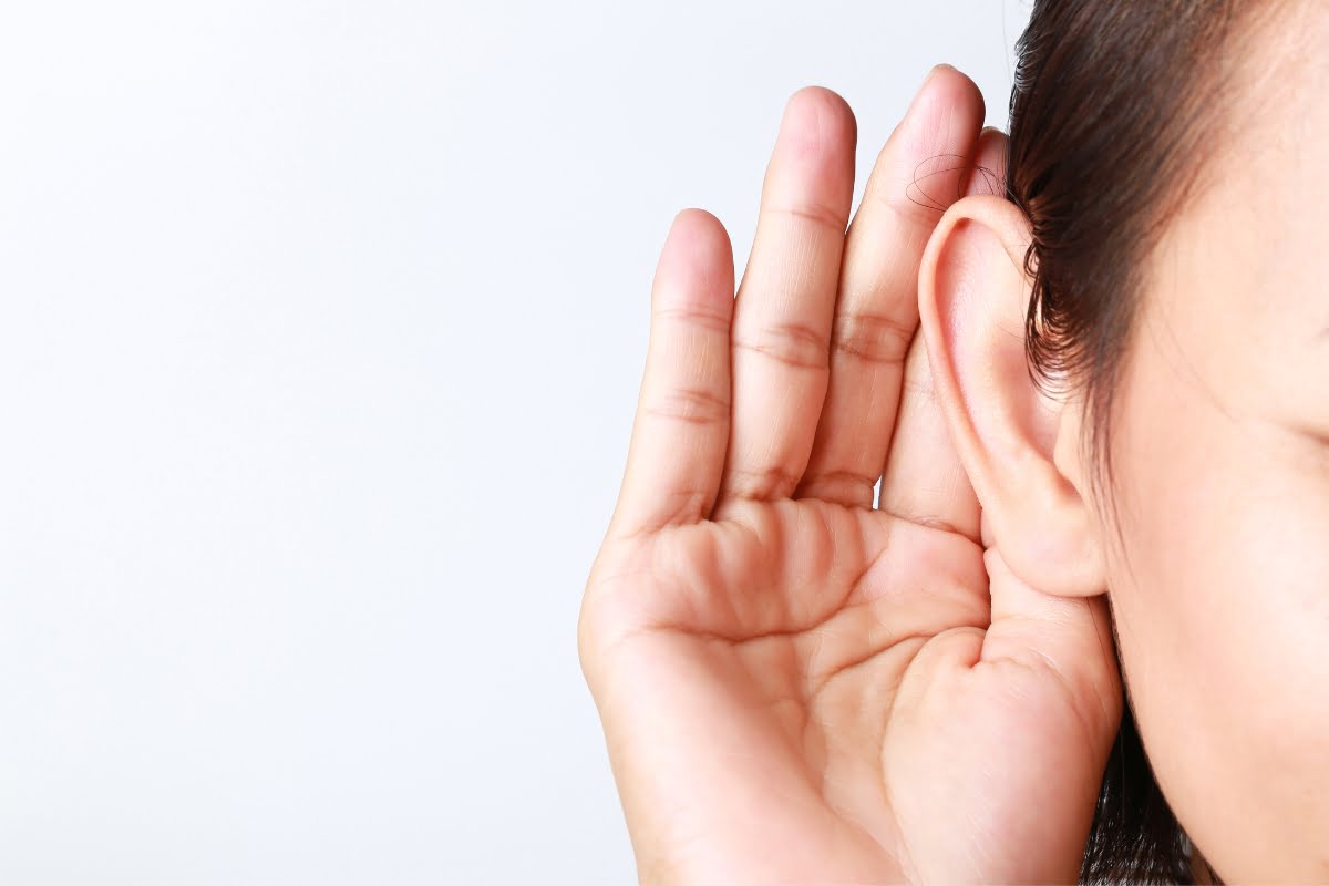 A person holds their hand to their ear, appearing to listen intently—embodying effective communication strategies. Only one side of their face and ear are visible against a white background.