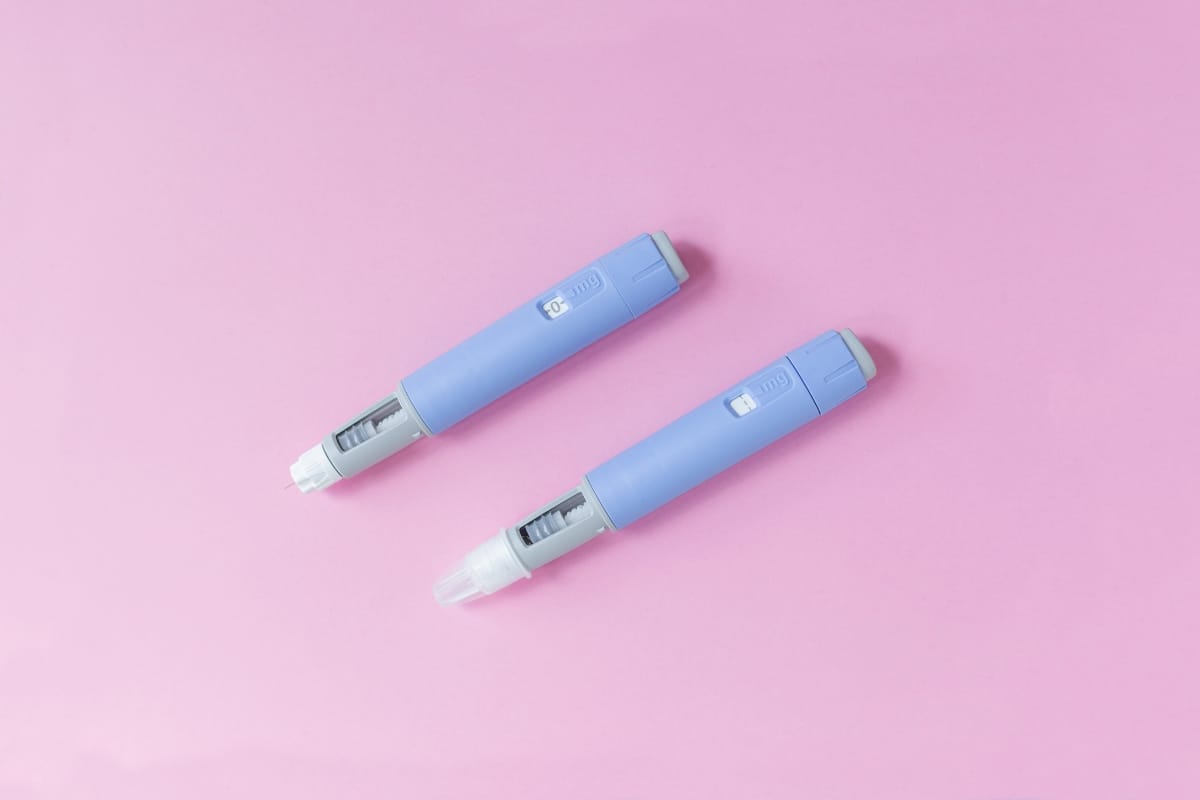 Two blue medical insulin pens, often considered part of weight loss solutions, lie parallel on a pink surface.