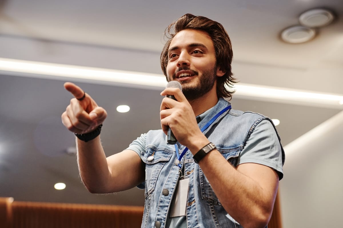 A person with a beard holds a microphone, gesturing passionately as one of the keynote speakers for business events.