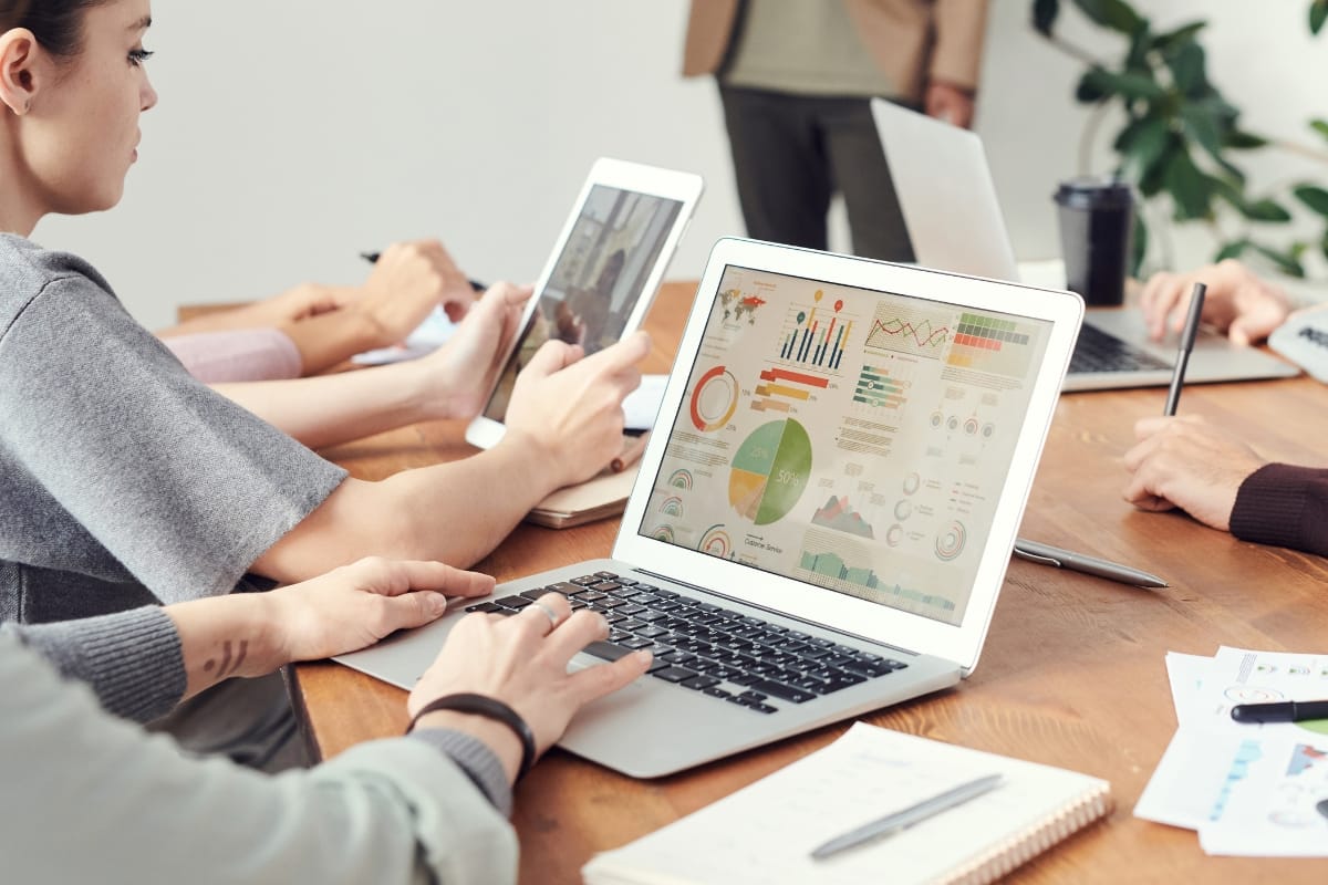 Leaders engage in problem-solving as they delve into charts on laptops and tablets, with notepads scattered across the meeting room table.