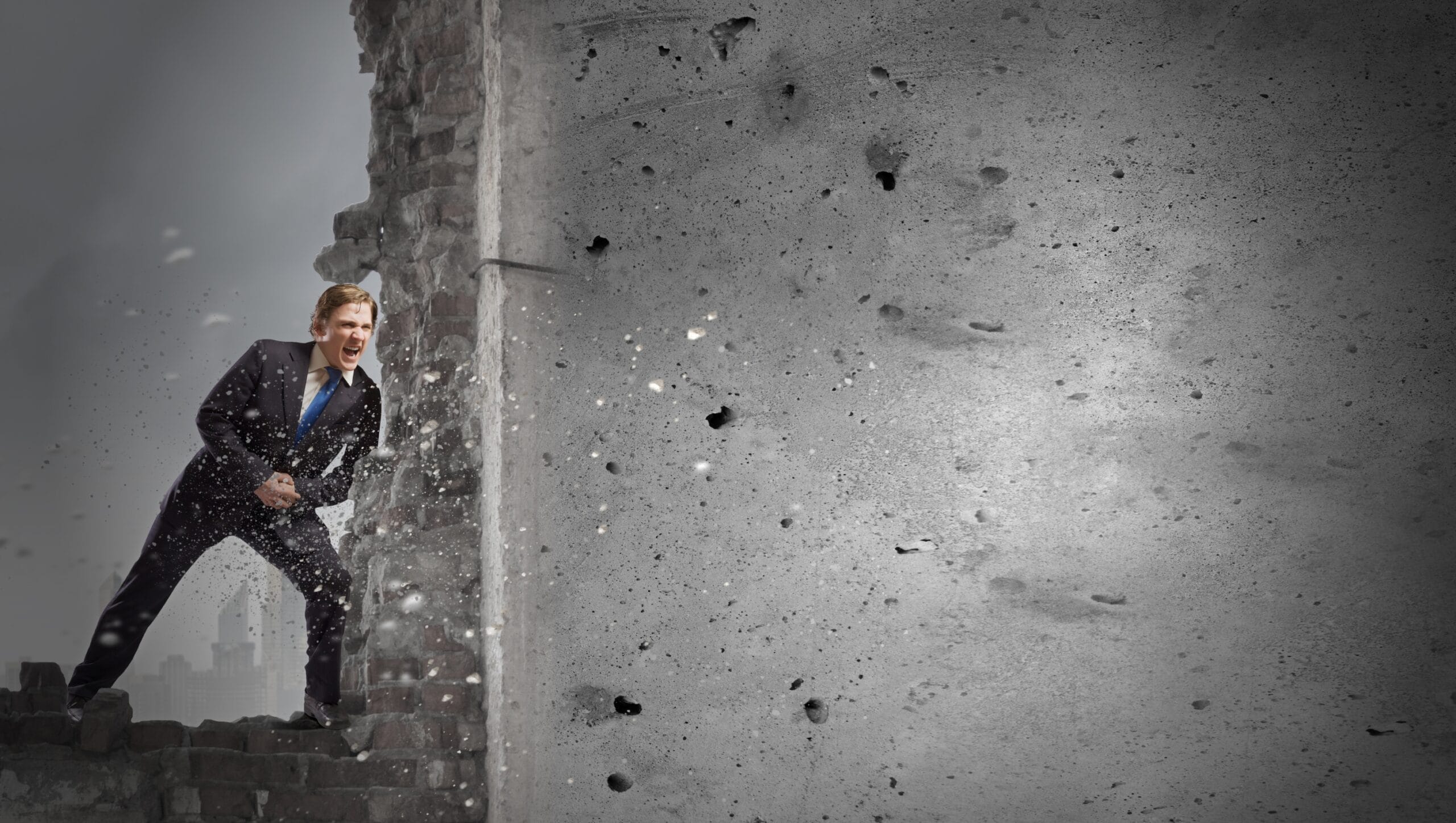 A man in a suit breaks through a brick wall, with debris flying around him, symbolizing the breakthroughs possible with Mind-Body Psychotherapy, against a gray background.