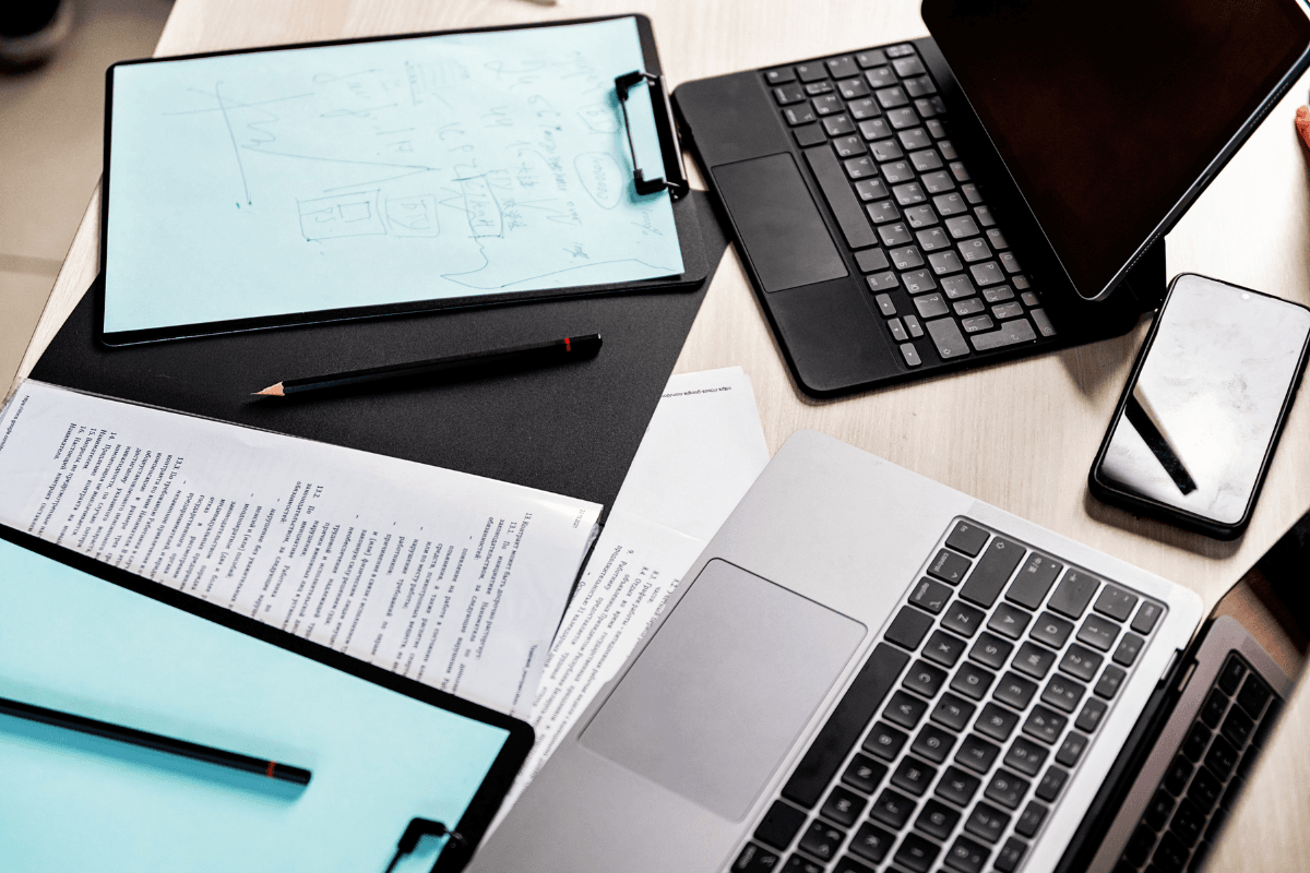 A desk with a laptop, tablet, smartphone, clipboards, printed documents, and pencils arranged in a workspace setting reflects mindful leadership and purposeful organization.