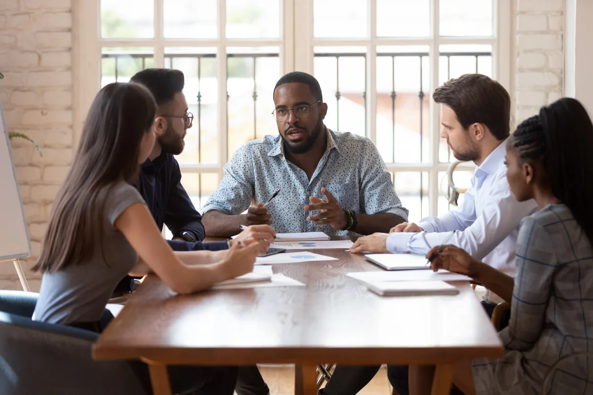 Five people sit around a table in a meeting room, discussing documents and charts, as one person demonstrates mindful leadership while the others listen attentively.