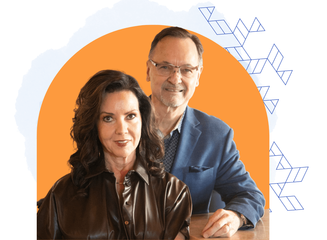 A woman in a brown leather shirt sits consulting with a man in a blue suit and glasses, both facing the camera with a geometric design and orange backdrop behind them.